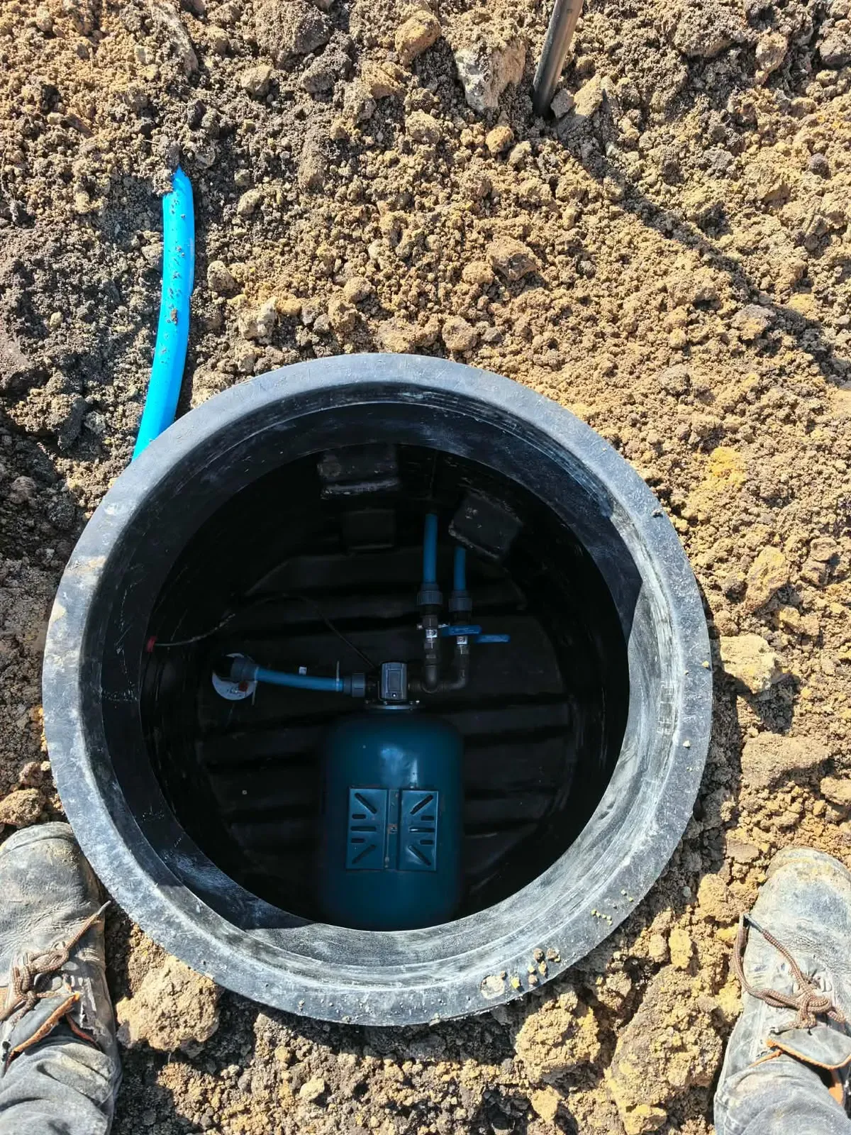 Widok z góry do obudowy studni z niebieskim zbiornikiem hydroforowym i rurą